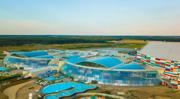 Największy aquapark w Polsce z błękitnymi dachami i kolorowym budynkiem. Widać baseny, zjeżdżalnie i plac zabaw.