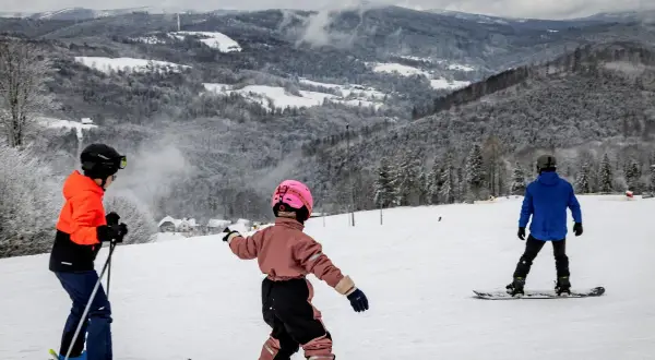 Dzieci na nartach i snowboardzie cieszą się zimowymi atrakcjami. Wspaniałe widoki górskie i śnieg zachęcają do aktywnego wypoczynku. Ferie 2026 lubuskie to idealny czas na takie przygody.