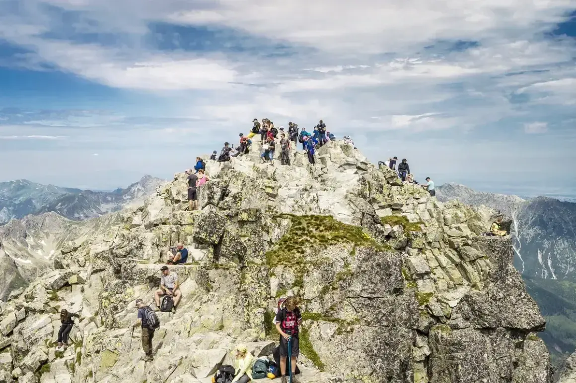Tłum turystów na skalistym szczycie Rysów, najwyższego szczytu w Polsce. Widok na Tatry.