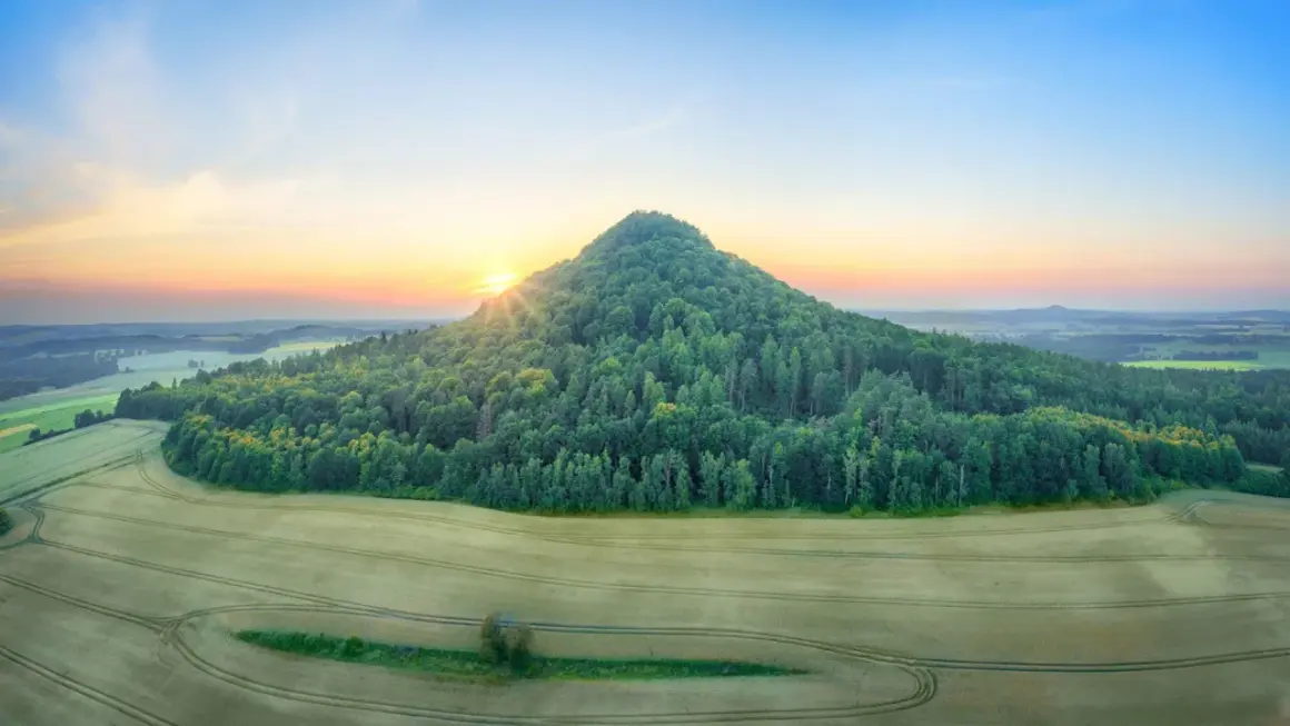 Góry Kaczawskie o wschodzie słońca. Stożkowaty, zalesiony szczyt góruje nad polami.