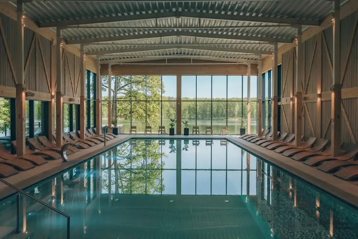Basen w nowoczesnym spa z widokiem na jezioro. Drewniane leżaki i przeszklone ściany tworzą relaksującą atmosferę, idealną dla najlepszego spa w Polsce.