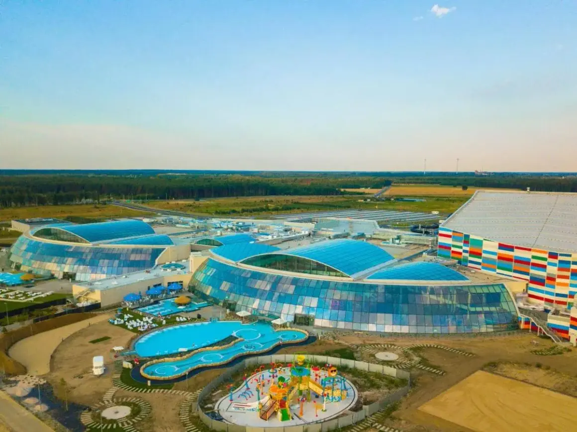 Największy aquapark w Polsce z błękitnymi dachami i kolorowym budynkiem. Widać baseny, zjeżdżalnie i plac zabaw.