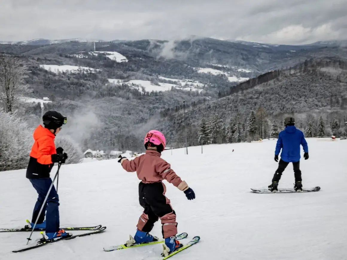 Dzieci na nartach i snowboardzie cieszą się zimowymi atrakcjami. Wspaniałe widoki górskie i śnieg zachęcają do aktywnego wypoczynku. Ferie 2026 lubuskie to idealny czas na takie przygody.