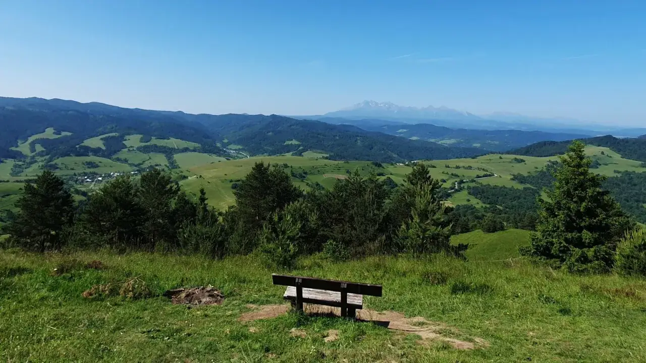 Ławka na przełęczy pod Tokarnią zaprasza do podziwiania zielonych wzgórz i odległych gór.