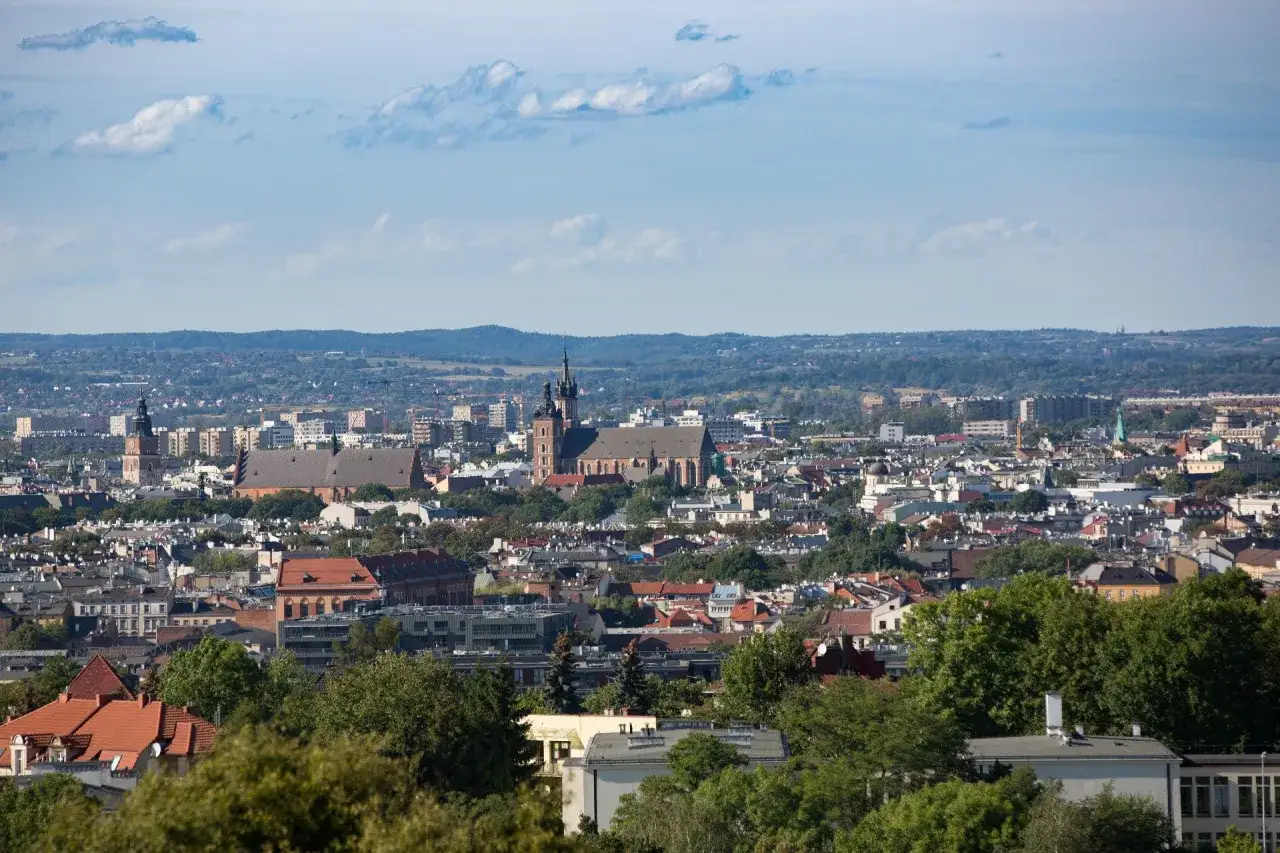 Panorama Krakowa z dominującymi kościołami i zielenią. Widać wiele dachów i budynków, tworząc obraz pięknych miejsc w Krakowie.