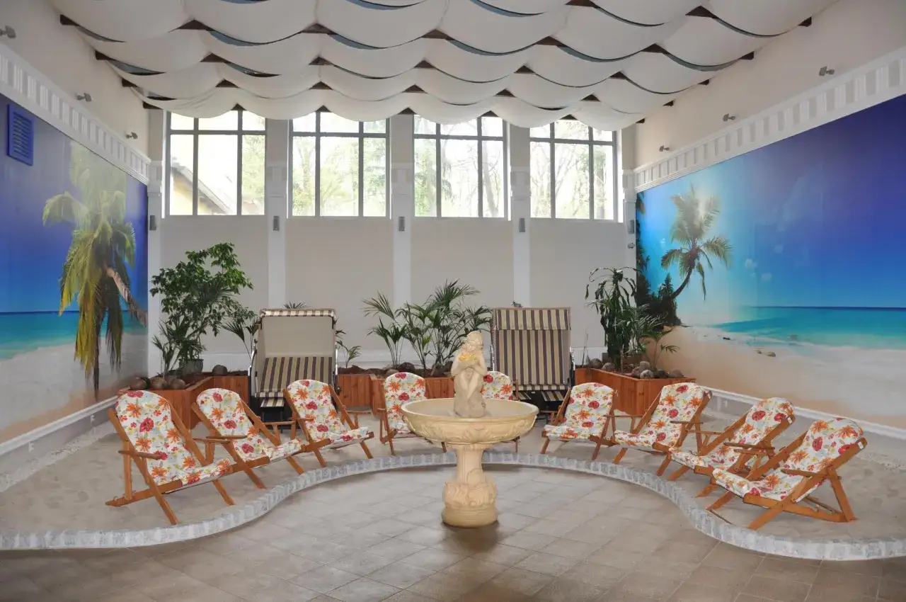 Wnętrze z piaskiem, leżakami i fontanną, ozdobione muralem plażowym. Idealne sanatorium godne polecenia dla relaksu.