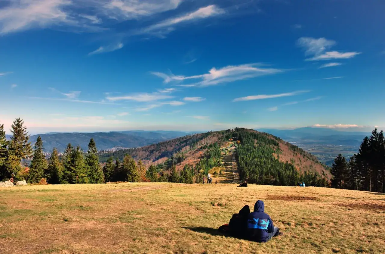 Widok na góry w Bielsku-Białej. Dwie osoby siedzą na trawie, podziwiając jesienny krajobraz i panoramę Beskidów.