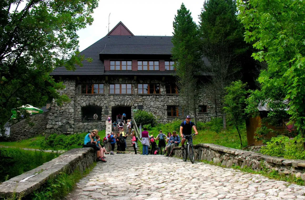 Kamienny schronisko w Dolinie Chochołowskiej, z turystami na brukowanym podejściu i rowerzystą.