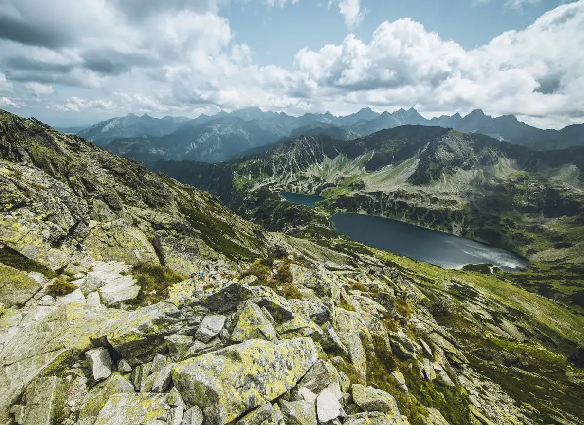 Widok z Kozi Wierch na Tatry. Kamienista ścieżka prowadzi w dół do dwóch jezior.
