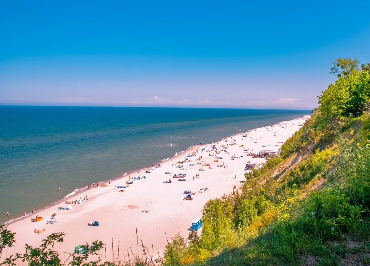 Piękna plaża z turkusową wodą i zielonymi klifami. Idealne miejsce, gdzie na wakacje, z mnóstwem ludzi odpoczywających na piasku.