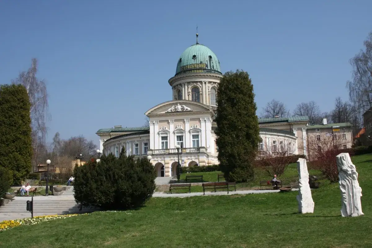Lądek Zdrój atrakcje: majestatyczny budynek z kopułą, zielony park, rzeźby i ławki zachęcają do odpoczynku.