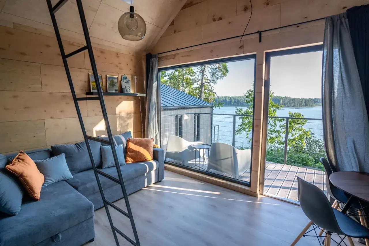 Przytulny salon z widokiem na jezioro, idealny na mazury z psem. Kanapa, drabinka i drewniane ściany tworzą domową atmosferę.