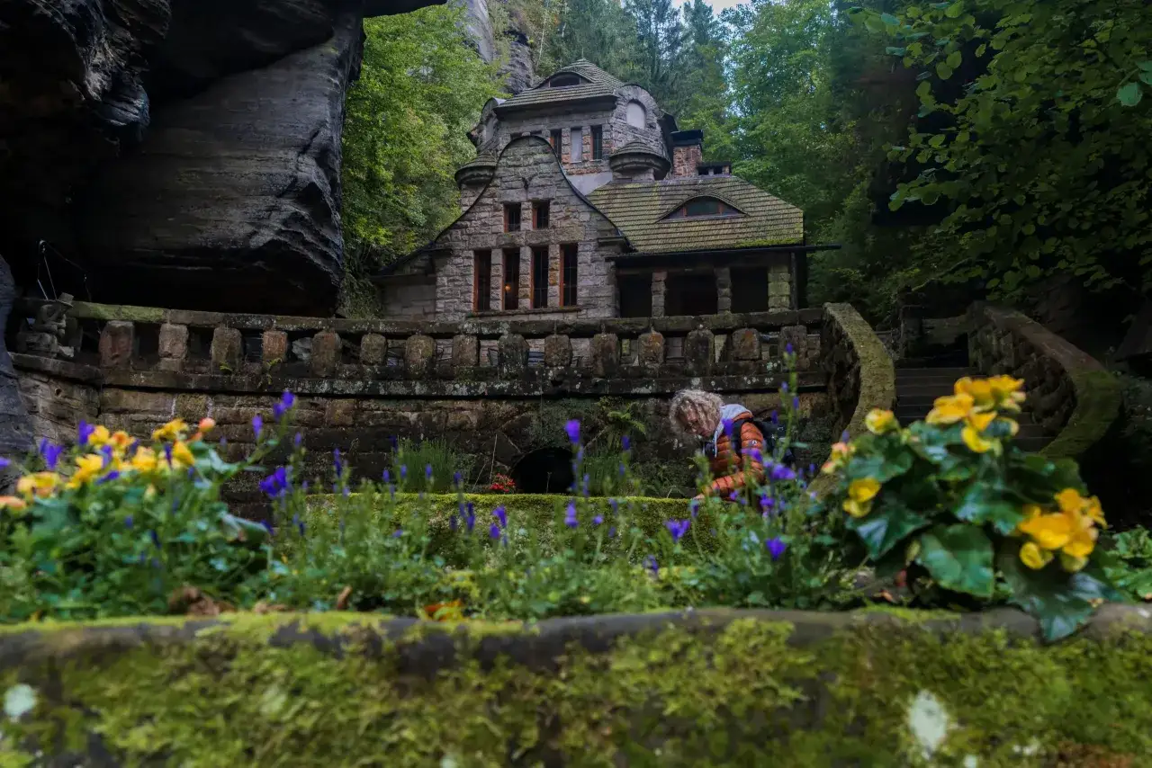 Kamienny domek w otoczeniu skał i zieleni, przypominający scenerię z Małej Szwajcarii Czech.