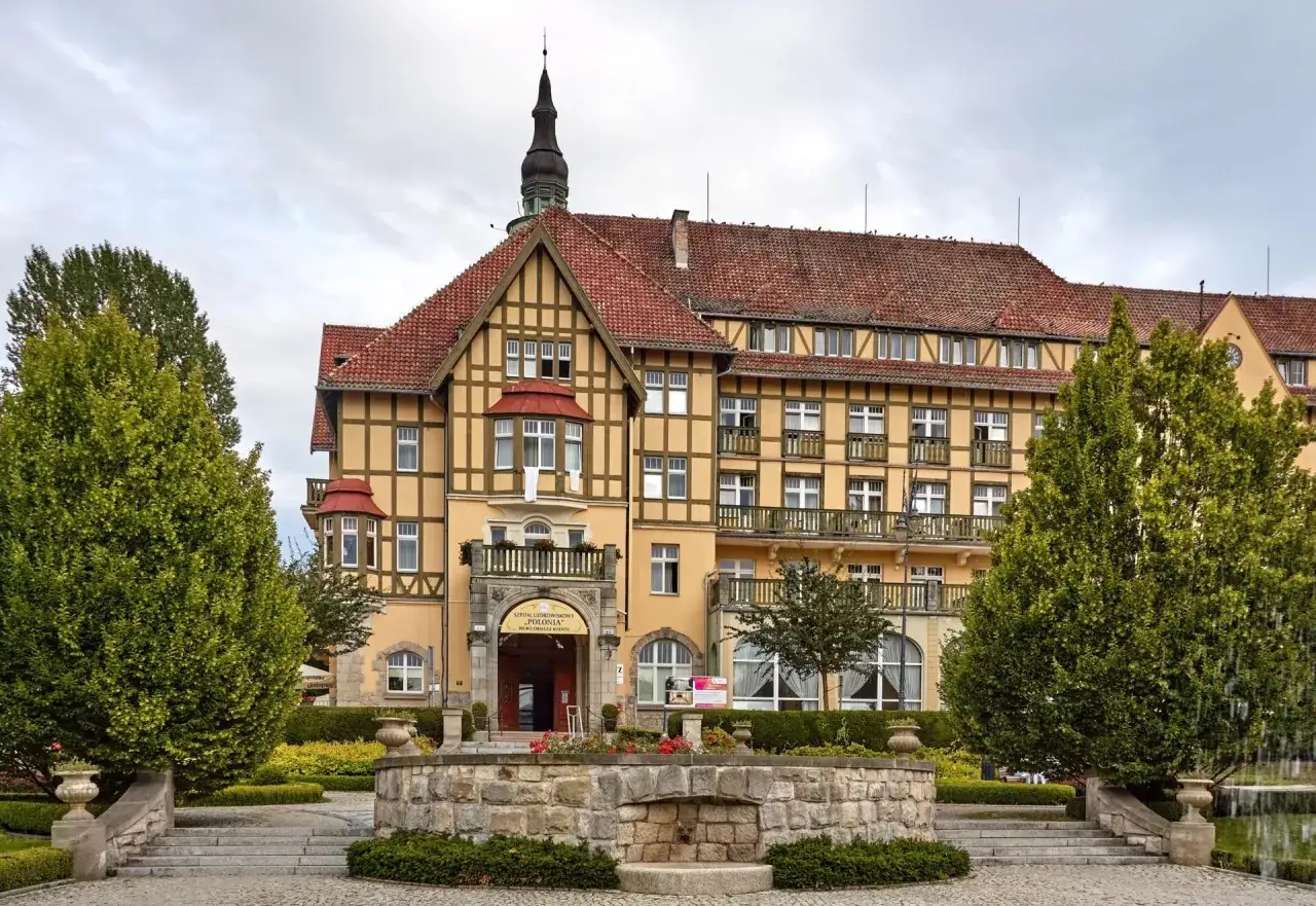 Piękny budynek szpitala uzdrowiskowego w Polsce, z charakterystyczną architekturą i zadbanym ogrodem.