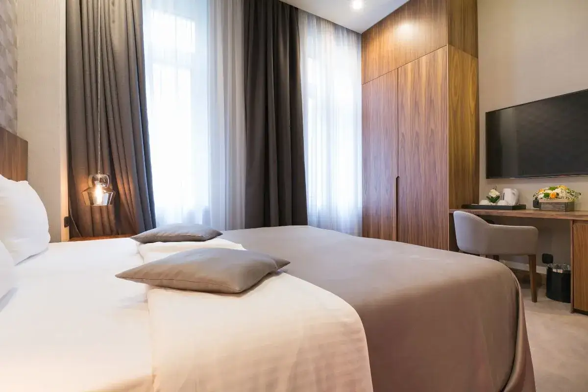 Elegancki pokój hotelowy z dwoma łóżkami, szafą z drewna orzechowego i telewizorem. Różne rodzaje pokoi hotelowych oferują komfort.
