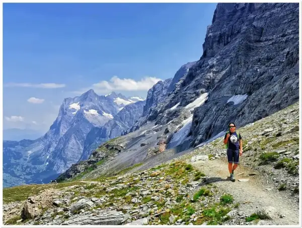 Wspaniały dzień na trekking w Alpach. Osoba z plecakiem idzie ścieżką wśród skalistych zboczy i ośnieżonych szczytów.