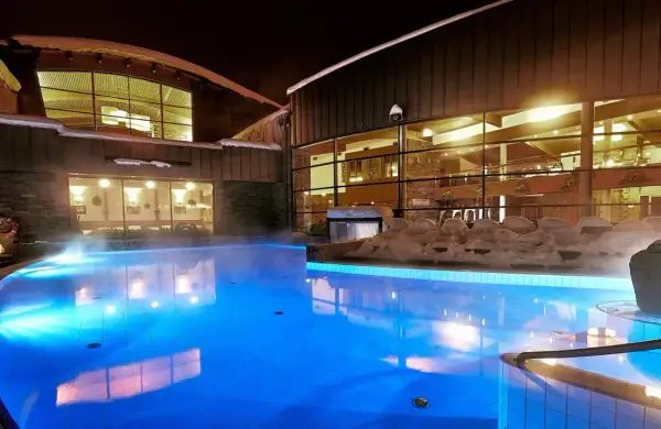 Nocą hotel z basenami termalnymi kusi błękitnym blaskiem wody i parą unoszącą się nad taflą.