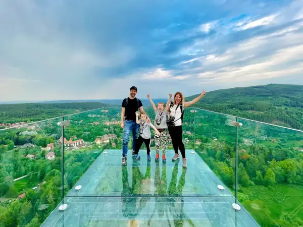 Rodzina na szklanym tarasie Sky Walk Świeradów Zdrój, podziwiająca malowniczy widok na góry i miasteczko.