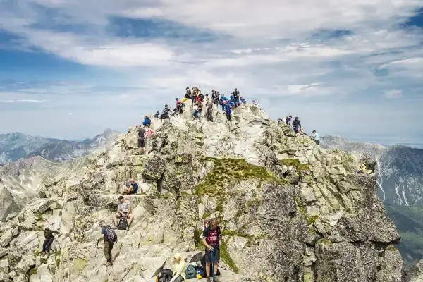Tłum turystów na skalistym szczycie Rysów, najwyższego szczytu w Polsce. Widok na Tatry.