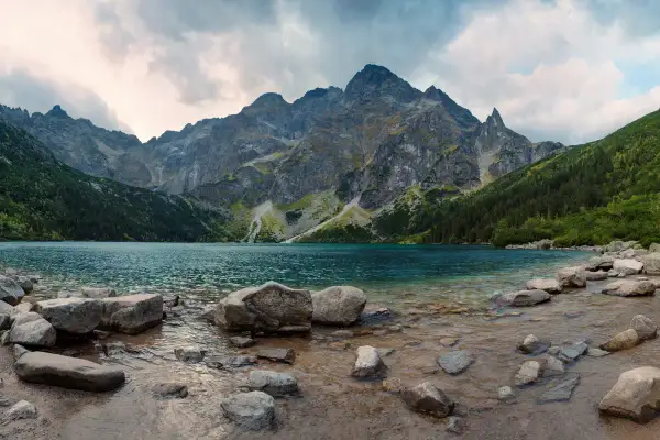 Spokojne jezioro otoczone stromymi górami i lasami. Widok na malownicze doliny w Tatrach, z kamienistym brzegiem.