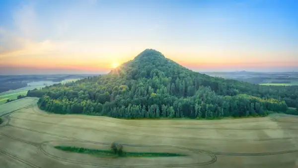 Góry Kaczawskie o wschodzie słońca. Stożkowaty, zalesiony szczyt góruje nad polami.