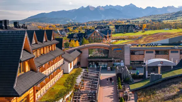 Drewniany hotel z pięknym widokiem na jesienne Tatry. W oddali widać góry i kolorowe drzewa.
