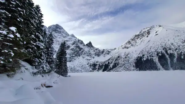 Morskie Oko zimą. Zamrożone jezioro otoczone ośnieżonymi szczytami i gęstym lasem świerkowym.
