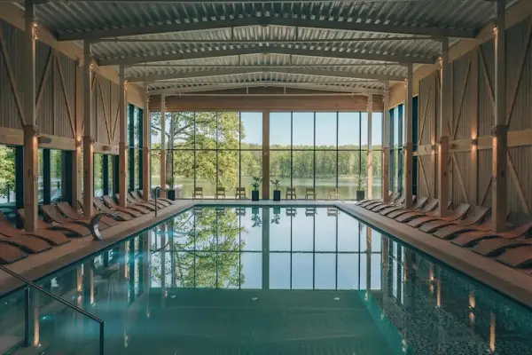 Basen w nowoczesnym spa z widokiem na jezioro. Drewniane leżaki i przeszklone ściany tworzą relaksującą atmosferę, idealną dla najlepszego spa w Polsce.