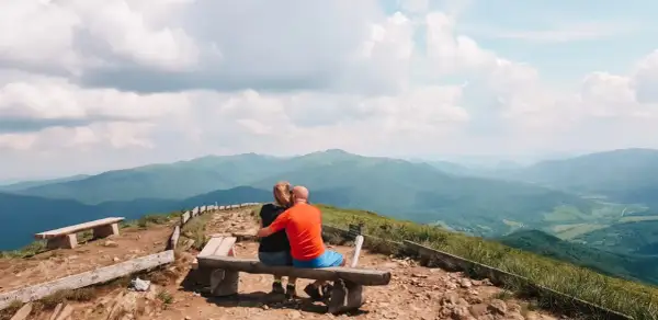 Para zakochanych na ławce podziwia bezkresne, zielone połoniny. Bieszczady jakie to góry – łagodne, rozległe, pełne spokoju.