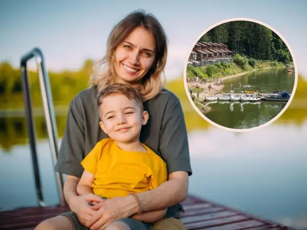 Uśmiechnięta mama z synkiem na pomoście, w tle jezioro z łódkami i domkami. Idealne miejsce na wakacje z bonem turystycznym.