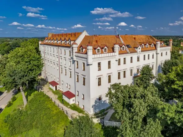 Biały zamek z czerwonym dachem, otoczony zielenią, to jeden z urokliwych zamków hoteli w Polsce.