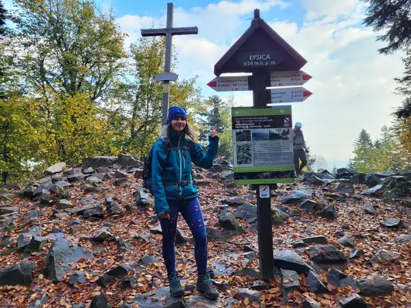 Kobieta na szczycie Łysicy, najniższej góry w Polsce (614 m n.p.m.). Jesień, liście, krzyż i drogowskazy.