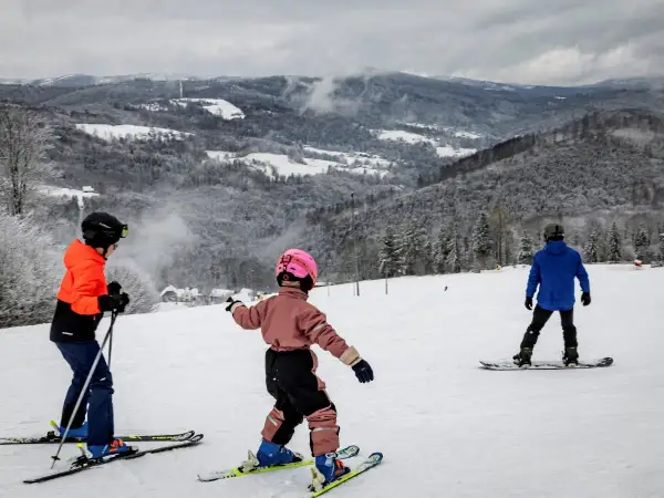 Dzieci na nartach i snowboardzie cieszą się zimowymi atrakcjami. Wspaniałe widoki górskie i śnieg zachęcają do aktywnego wypoczynku. Ferie 2026 lubuskie to idealny czas na takie przygody.